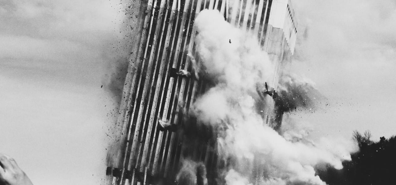 A black and white photo of a building engulfed in flames, with smoke billowing into the sky