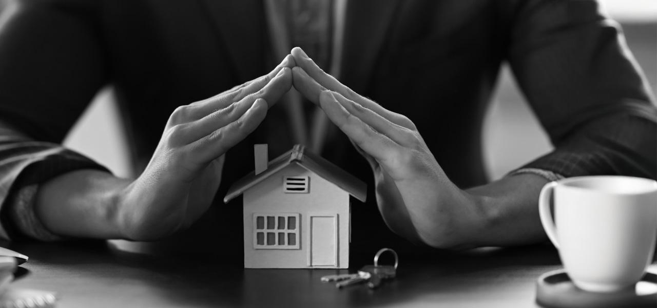 A man in a suit proudly holds a small model of a house