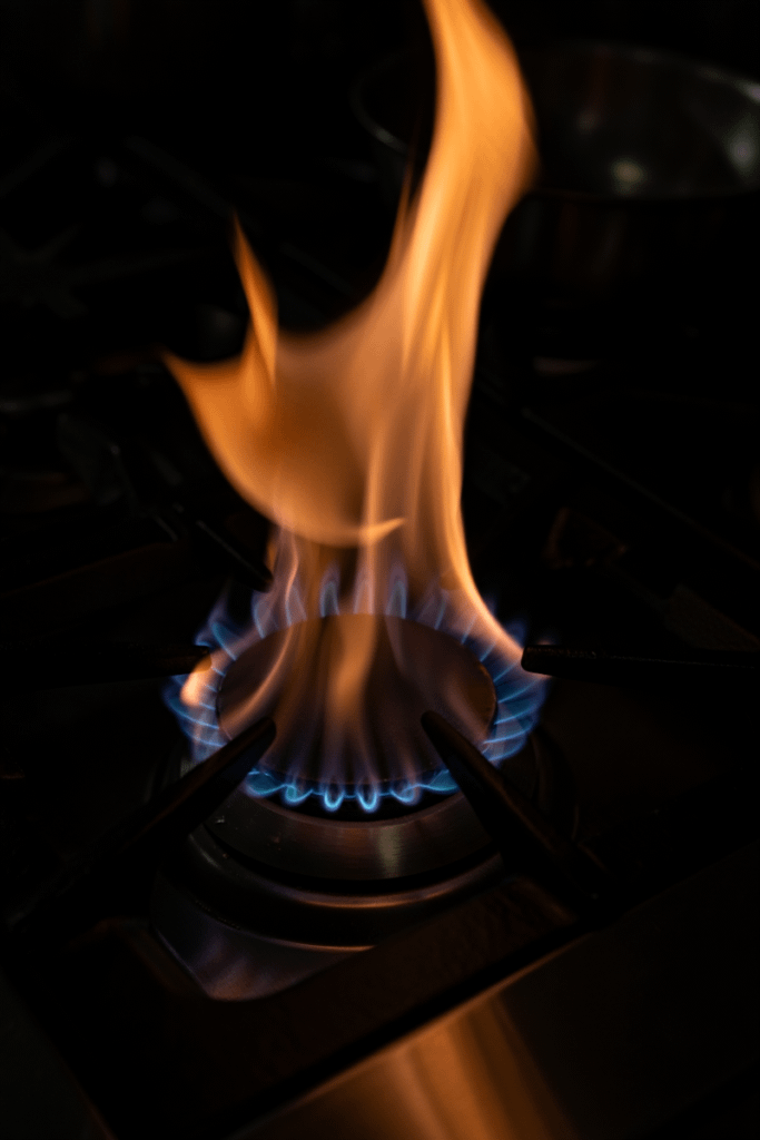 Close-up of a gas stove burner with a vibrant blue and orange flame, set against a dark background for dramatic contrast.