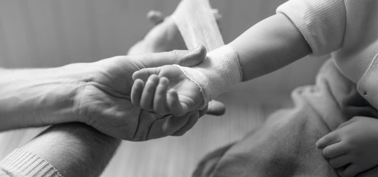 A black and white photo of an adult gently putting crepe bandage on a child's arm