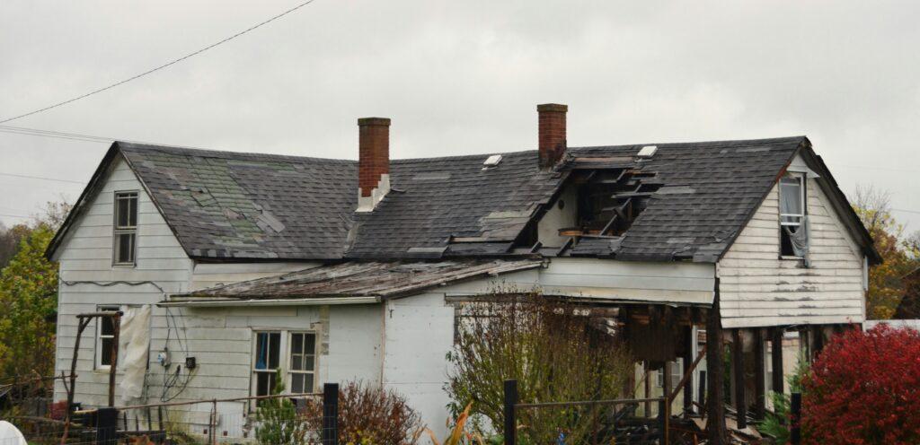 A house with charred walls and a collapsed roof, showing significant damage from a recent fire.