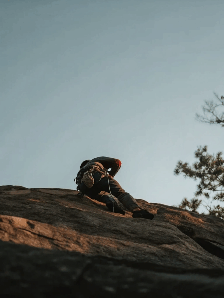A climber ascends a sunlit rock face with safety gear