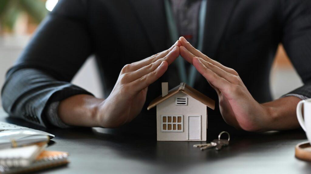 a person forms a roof with their hands over a model house