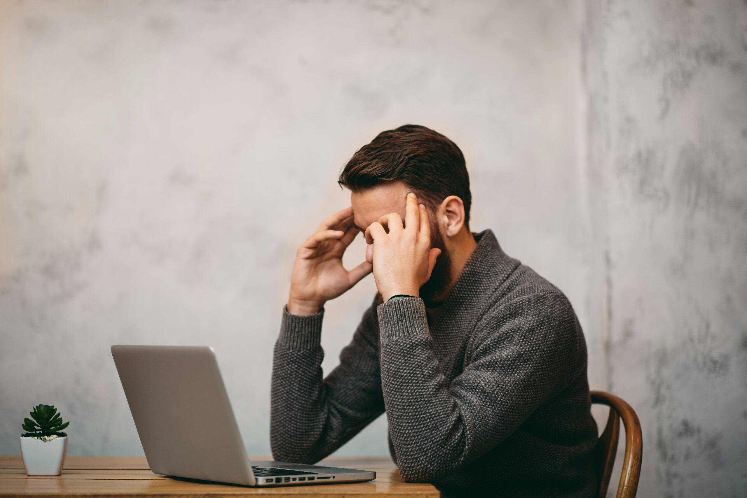 A man sitting at a table, resting his head in his hands, appears deep in thought or distress.