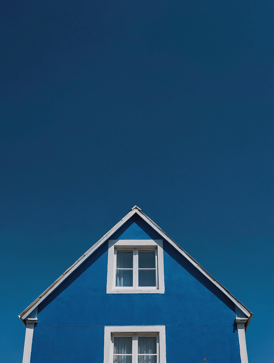 Bright blue house with white trim and windows against a clear deep blue sky, creating a striking and minimalistic visual contrast.