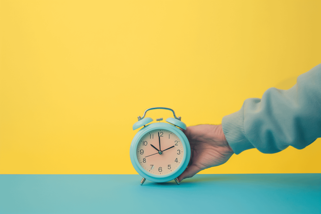 Light blue alarm clock held against a yellow background, showing 10:10. Contrasting turquoise surface adds a vibrant touch.